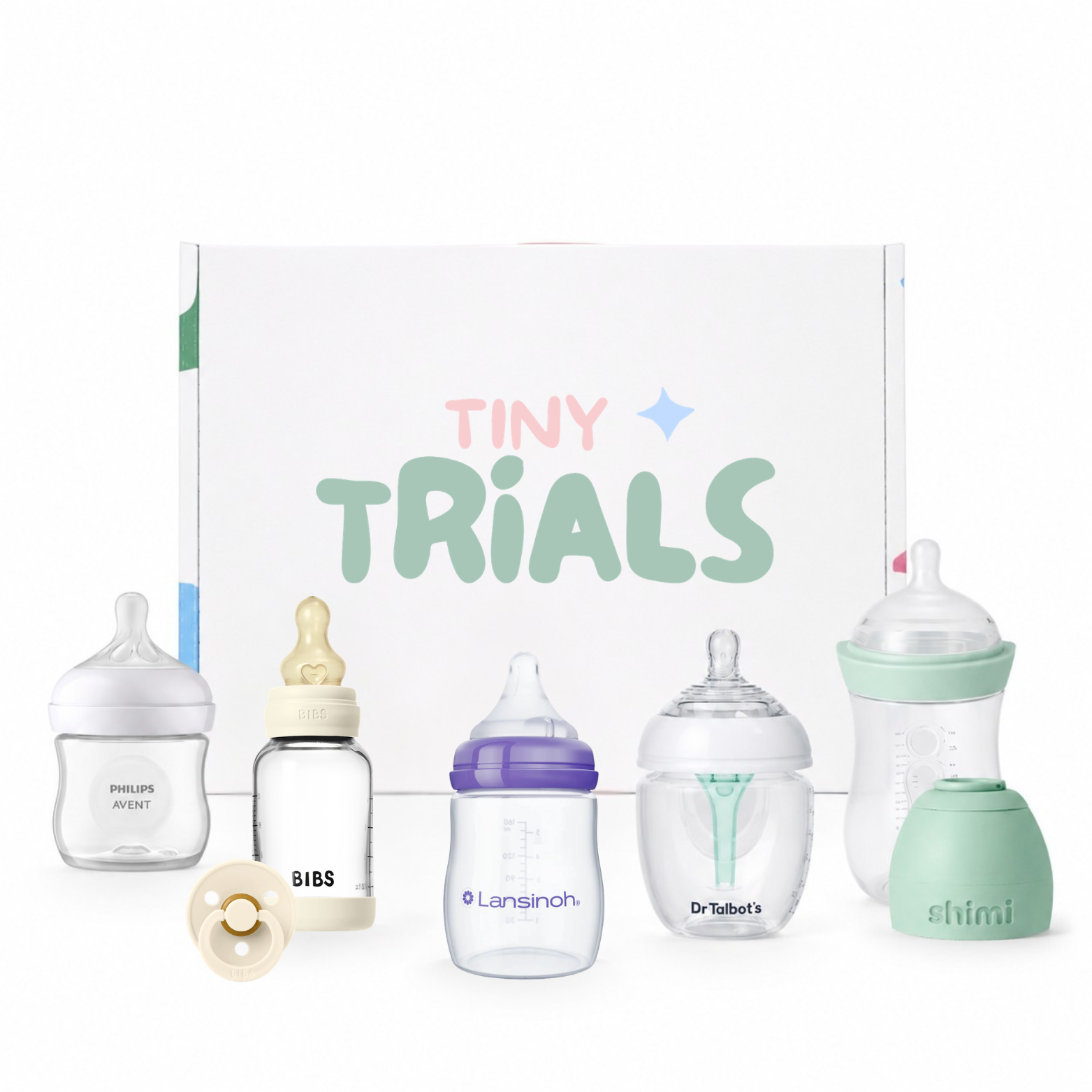 A baby bottle set displayed in front of a branded white box labeled 'TINY TRIALS.' The set includes multiple transparent bottles with different colored nipples and caps, plus matching silicone bottle covers, arranged on a clean white background.